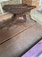 An antique iron anvil resting on wooden surface with visible rust and wear. The image shows the entire side profile with tapered horn clearly visible.