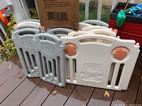 Plastic playpen panels stacked together showing neutral colors, bear faces, and flower accents.