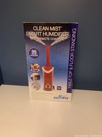 Front view of the boxed Clean Mist Smart Humidifier showing product name, runtime, and compatibility for tabletop and floor use.