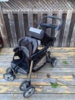 Full side view of double stroller showing front and rear seats, wheels, and standing platform.