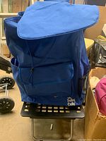 Front view of blue trolley dolly with closed flap storage bag on black plastic base with metal frame and wheels.