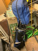 Blue and black golf bag upright with attached stand closed with top cover, filled with golf clubs