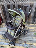 Full view of Graco stroller showing canopy, padded seat with striped fabric, child tray with cup holder, and four wheels on wooden deck surface.