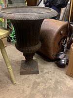 Front angle view of the antique cast iron garden urn showing the flared rim, pedestal base, and detailed decorative motifs.