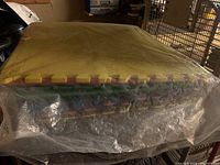 Stack of multicolored kids floor mat squares packed in a plastic bag, showing colors yellow, green, blue, and red, viewed from side and top angles.