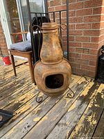 Front angled view showing the full chiminea with its tall chimney, wide open fire chamber, and ornate cast iron feet on a worn wooden deck.