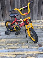 Full view of Tonka Monster X12 kids bike in red, yellow, black with training wheels on wooden deck