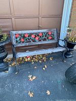 Full view of cast iron garden bench with decorative painted floral design on backrest and wooden slats on seat. Bench shows wear with peeling and missing wood slats.
