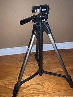 Front view photo of Velbon CX440 tripod standing on wooden floor showing tripod legs and head with pan-tilt handle and Velbon branding.