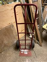 Front view of red tall dolly with metal frame, two inflated wheels, and attached white rope.