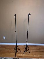 Front view of two black collapsible microphone stands extended, showing tripod bases and microphone clips attached at top.