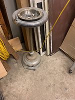 Full view of the tall vintage metal ashtray, showing the base, slender column, and ashtray insert top with a missing piece.