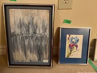 Two framed artworks displayed together on a beige wall: a larger abstract painting on the left with a gray frame and a smaller floral print with a blue mat and silver frame on the right.
