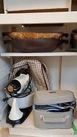 Shelf with two wooden baker dishes, white Oster hand mixer with power cord and beaters, gray soft carrying case with knives inside.