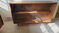 Front view of wooden two-shelf bookcase with sliding glass doors in sunlight.