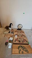 Photo showing four wooden fish boxes with smoked salmon artwork, one wooden box with carved fish, decorative eggs, decorative fans, stuffed duck, and Mexican obsidian figurine on carpeted floor against wall.
