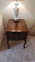 Full view of the wood end table with lamp on top, showing scalloped top and curved legs.