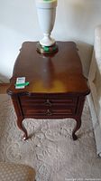 Front view of the wooden end table showing the dovetailed drawer and curved top edges with a lamp placed on it.