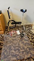 Photo showing the C.C.M exercise bike alongside the exercise mat and jump ropes on a brown patterned carpeted floor.
