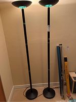 Two tall, matching black torchier floor lamps standing next to each other against wall.