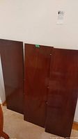 Three wooden table leaves leaning against wall, noted scratches and finish wear.