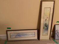 Both framed and matted art prints displayed against a wall, one vertical floral and one horizontal landscape.