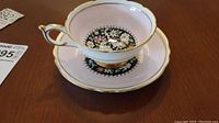 Side view of the white teacup and saucer with floral black medallion pattern and gold trim on the cup handle and edges