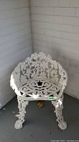 White painted metal patio chair with decorative leaf and scroll work on backrest, seat, and legs, shown from front corner view.