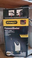 Box front showing Stanley pressure washer image, 1600 PSI, 1.4 GPM specification and assembly steps.