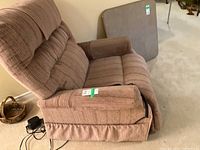 Side angle view of brown recliner lift chair showing padded armrest, seat, and backrest upholstery. Chair skirt base and remote wire visible.