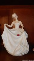 Front view of the Royal Doulton Tracy A porcelain figurine displaying the woman in a strapless gown holding the skirt with one hand and a pink rose detail on the dress.