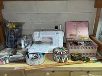 Front view of Kenmore sewing machine on shelf with sewing supplies including tin containers and a weaving box.