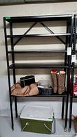 Front view of black metal shelving unit with four shelves and some miscellaneous items placed on the shelves for staging only. Shows unit is freestanding and including cross-bracing on the back.
