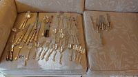 Full view of the flatware spread on a beige textured fabric, includes spoons, knives, forks with ornate Regency Plate handles.