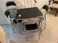 Full view of foldable metal table with four matching foldable chairs in black vinyl cushions and chrome metal frames.