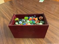 Wooden rectangular case filled with multicolored marbles, viewed from above at an angle