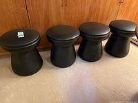 Four black leatherette swivel stools lined up against wood panel wall, showing entire lot.
