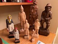 Full group of nine carved wood figures on shelf, varying sizes and styles