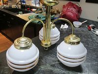 Chandelier with 3 white glass globes with gold stripes on a granite countertop showing front angle.