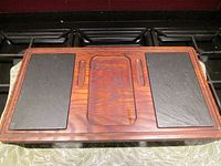 View of Baribo cheese board showing rectangular shape, integrated handles, wood grain, and two inset black tiles on a stove top.