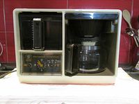 Front view of the cream-colored GE Spacemaker coffee maker showing the water reservoir, timer dial, control switch, and a glass carafe in the brewing area.