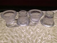 Four textured clear glass candleholders displayed in a row showing varied shapes and size proportions.