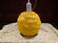 Yellow spherical pendant light made of heavy-duty plastic, showing the textured appearance resembling folded ribbons.