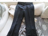 Front view of black ski pants laid flat on a couch showing zip front and overall style.