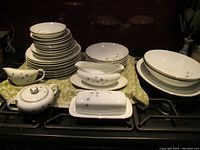 Stacks of plates, bowls, gravy boat, creamer, sugar bowl, covered butter dish on stove top