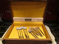 Interior view of the open wooden cutlery box lined in yellow fabric showing 7 forks and 6 spoons laid inside with Oneida label on lid interior.