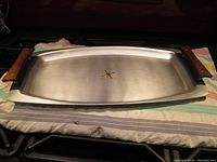 Full tray showing rectangular metal surface with raised teak handles and gold starburst in center