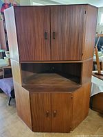 Full view of the assembled three-piece teak corner cabinet showing top and bottom sections with doors and open center.