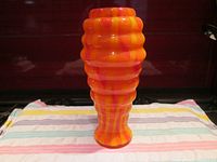 Front view of vibrant orange, red, and yellow beehive shaped glass vase on striped cloth background.