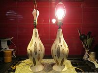 Pair of illuminated mid century modern table lamps on kitchen counter, showing front view and shape.